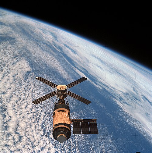 The Skylab space station with its solar panels, photographed in orbit above white clouds